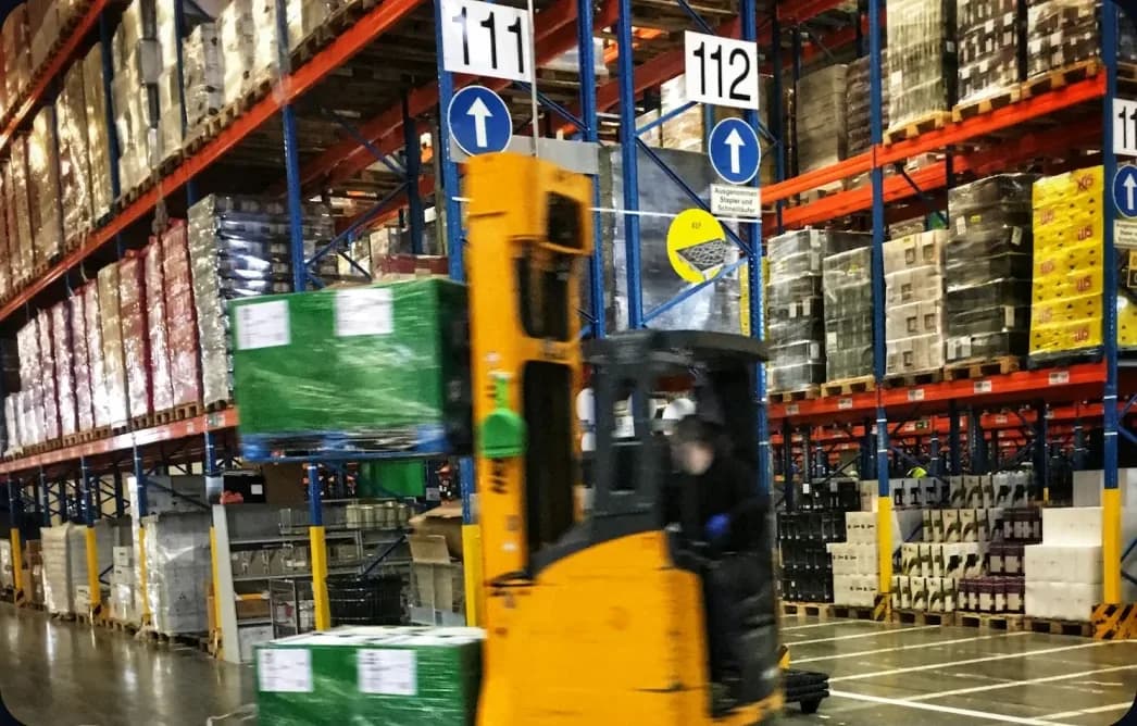 A forklift moving pallets between high-bay racks in a distribution warehouse