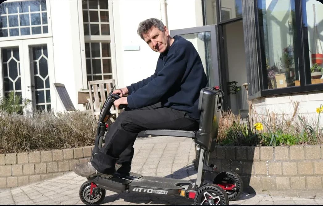 A man seated on a folding mobility scooter outside a house